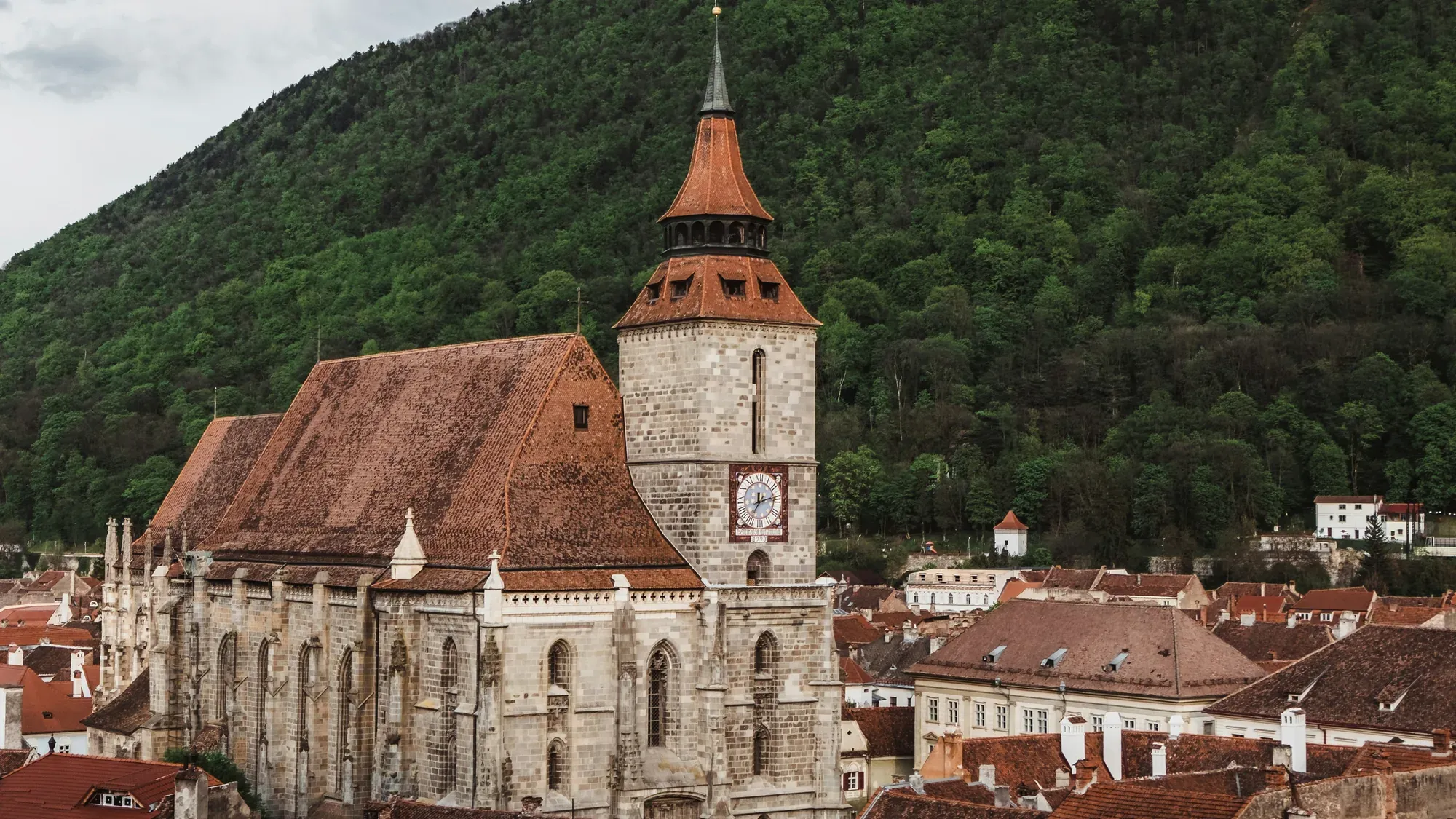 The Black Church in Brașov, its clock tower and tiled roof against the wooded slope of Tâmpa hill