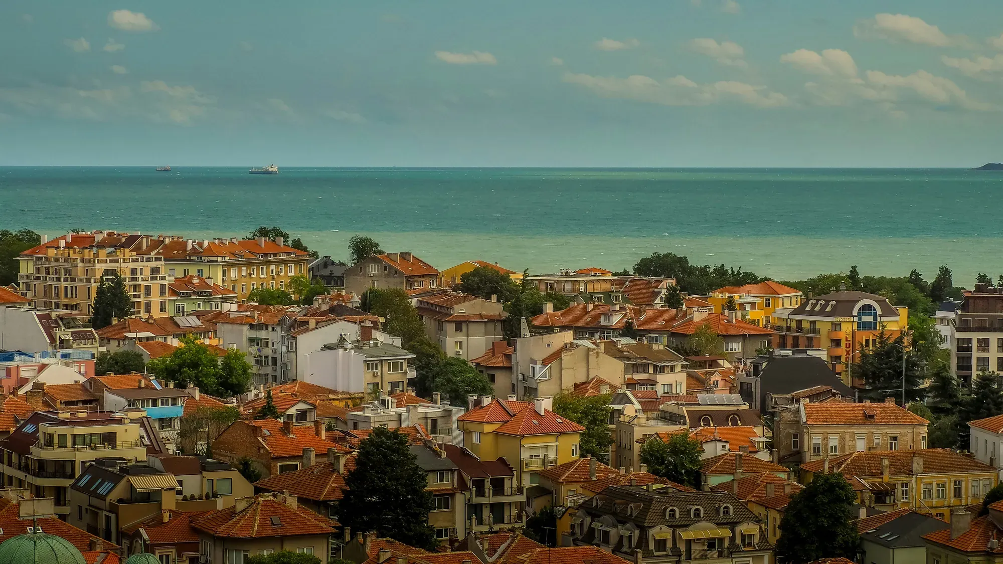 Tiled rooftops of Burgas running down to the Black Sea, with a cargo ship on the horizon